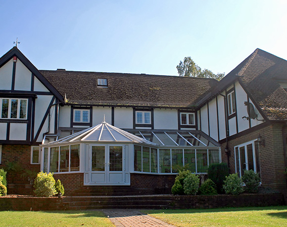 two-story house with a glass conservatory surrounded by greenery on a sunny day offering a spacious outdoor view featuring seven windows and well-maintained landscaping
