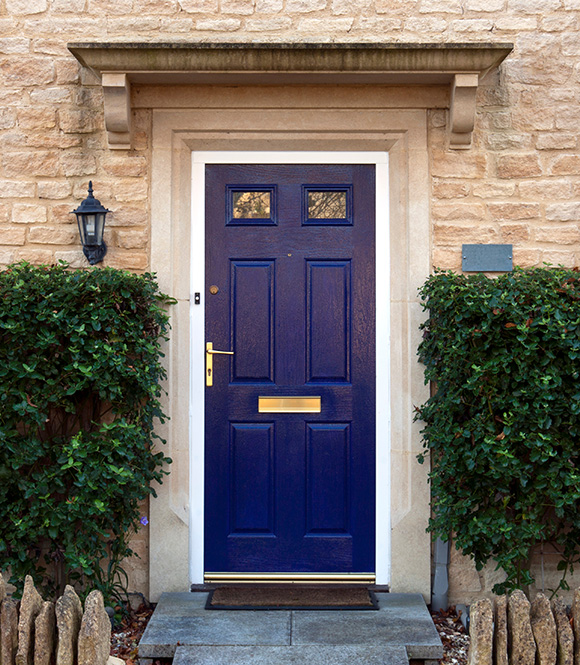 a blue front door with a golden handle and two small windows surrounded by green shrubs and a stone wall representing inviting home entrance and five architectural elements