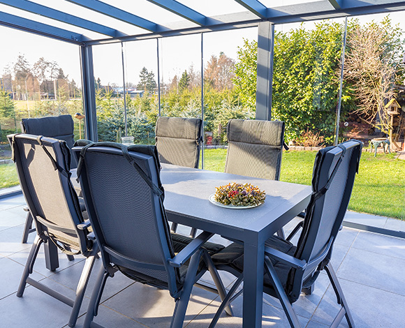 outdoor dining area with six chairs around a gray table adorned with a decorative plate on a sunny day featuring a green garden background perfect for enjoying meals with friends and family in twelve delightful settings